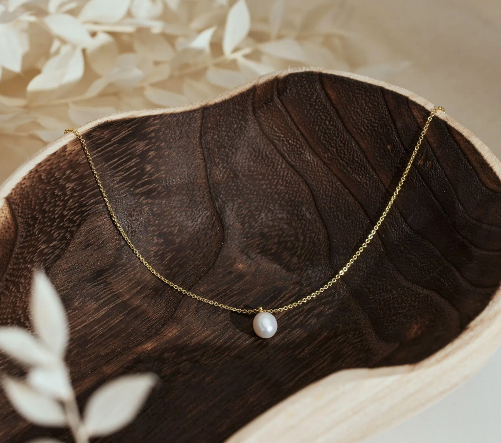 Gold necklace with a pearl pendant on a wooden surface