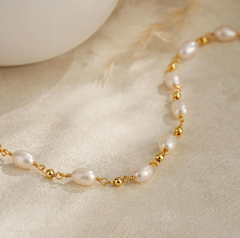 Pearl necklace with gold beads on a beige surface