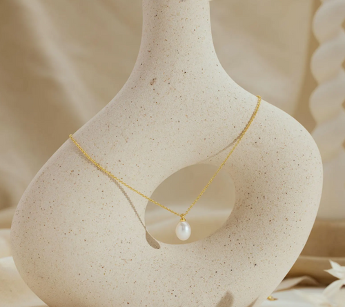 Gold necklace with a pearl pendant on a beige stone surface